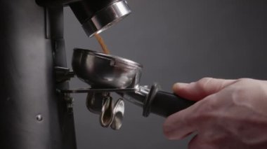 Kahve makinesine yakın çekim için portafilter dökülüyor. Bilinmeyen barista el ele tutuşan filtre dolu kahveyi çok yavaş çekimde öğütüyor. Profesyonel elektrikli öğütücü içecek için toz hazırlıyor.