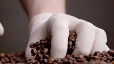 Hands wearing white gloves taking handful coffee seeds close up. Unknown person checking quality roasted aromatic beans closeup. Perfect brown grains ready to grinding for energetic beverage.