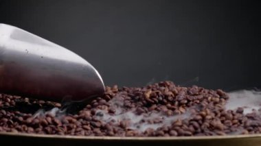 Metal küreği karıştıran kahve çekirdekleri. Çelik kepçesi çok yavaş çekimde kahve çekirdeği alıyor. Karanlık arka planda sıcak aromatik tohumların üzerine yükselen buharı kapat. Aroma arabica kavramı.