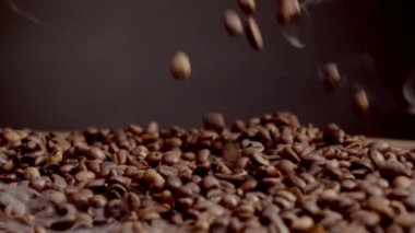 Kokulu kahve çekirdekleri yığının üzerine dökülüyor. Aromatik kahve çekirdekleri koyu arkaplan üzerine dökülüyor. Kahve tanelerini ağır çekimde kavururken hafif buhar. Enerji içeceği içeriyor..