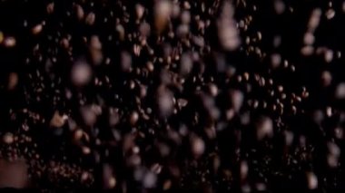 Natural coffee grains jumping up in super slow motion. Fantastic splash roasted aromatic beans on black background. Fragrant fresh coffee seeds flying close up. Organic arabica robusta concept.