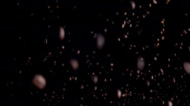 Flying of delicious coffee grains on dark backdrop. Aromatic caffeine beans rising up falling after exploding in super slow motion. Fragrant fresh coffee seeds downfall on black background close up.