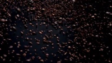 Beautiful downfall roasted coffee seeds close up. Fresh aromatic beans falling on black background in super slow motion. Fragrant brown grains flying on camera. Cafeteria cafe design concept.