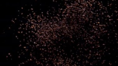 Super slow motion of roasted coffee grains exploding flying away. Closeup aromatic arabica seeds falling on camera. Beautiful view fragrant coffee beans splashing on black background. Caffeine product