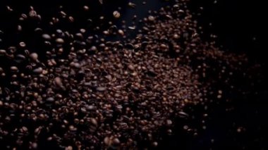 Exploding aromatic coffee grains in super slow motion. Roasted fragrant seeds for tasty drink splashing on black background. Beautiful view beans falling close up. Morning energetic beverage concept.