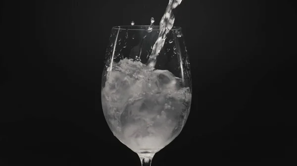 氷のワイングラスを注ぐウォータージェットの閉鎖 透明なガラスの中に氷のキューブと明確な泡の液体をスパークリング 空気で発泡固定ミネラルウォーターは黒の背景をドロップします カクテルコンセプトの準備 — ストック写真