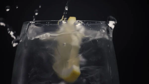 柑橘類の滝の水がガラスの閉鎖を落とした 氷のキューブとマクロでレモンスライスと冷たい水 透明なワイングラスに泡で飲み物を準備します カクテル作りとミクソロジーコンセプト — ストック写真