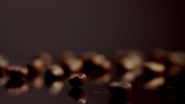 Closeup few coffee beans lying table super slow motion. One brown grain spinning on foreground. Roasted caffeine seeds grinding for energetic morning beverage. View of aromatic coffee harvest indoors.