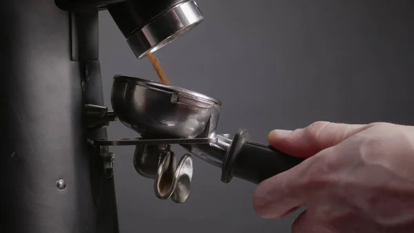 Ground coffee pouring in portafilter for coffeemaker closeup. Unknown barista hand holding filter fulling grinding coffee in super slow motion. Professional electric grinder preparing powder for drink