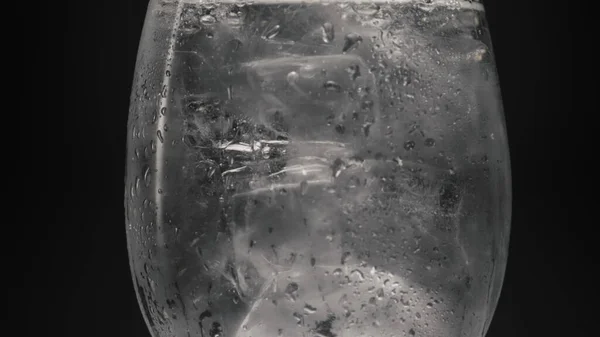 Ice blocks cold water glass closeup. Alcohol gin soda drink with ice cubes in wineglass sparkling slow motion. Cool clear beverage establishing black background. Refreshing tonic concept