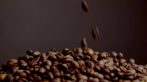 Aromatic coffee beans falling down on large heap closeup. Roasted brown grains pouring super slow motion. View of perfect fresh seeds for making morning espresso. Tasty coffee harvest on dark backdrop