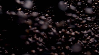 Falling fragrant coffee seeds on dark background. Super slow motion roasted aromatic grains for energetic morning drink. Beautiful downfall fresh brown coffee beans closeup. Cafeteria design concept.