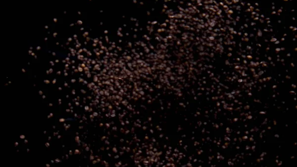 Coffee grains pile falling down on black background. Super slow motion of roasted fresh beans downfall. Close up coffee seeds flying on dark backdrop. Perfect ingredient for energetic caffeine drink.