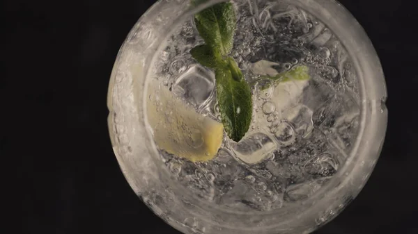 泡状のレモンアイスミントカクテルがガラスを閉じます 氷のキューブ輝くソーダ水超スローモーション 黒い表面の背景の上からのマクロビュー 夏のさわやかな冷たい飲み物のコンセプト — ストック写真