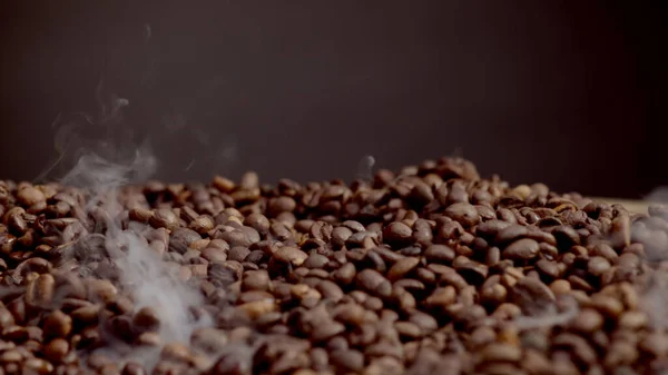 Vapor rising over hot coffee grains in super slow motion. Close up fragrant brown seeds roasting on dark background. Process preparing aromatic beans for energetic morning beverage. Arabica concept.