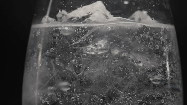 Frozen blocks sparkling drink glass closeup. Fizzy bubbled pure soda water in wineglass slow motion. Carbonated mineral aqua establishing black background. Refreshing cocktail concept