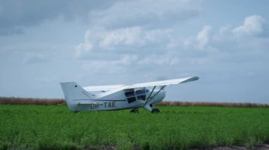 Propeller small airplane parking on green field after long transportation flight. Ultralight white plane with spinning blades turning off engine landing in summer farmland. Private aircraft transport.
