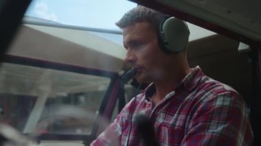 Middle age airman starting airplane engine sitting cockpit with headphones on head closeup. Portrait focused pilot looking camera making preflight checking small private plane in cabin. Flight concept