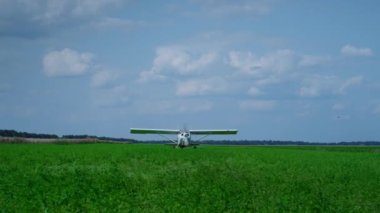 Lightweight airplane with spinning propeller parking on green field cloudy day. White small private plane landing after flight on beautiful farmland. View of working modern aircraft in front blue sky.