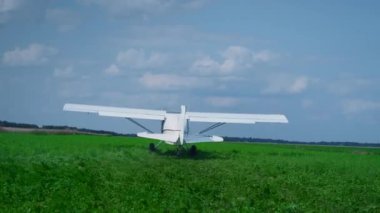 Small private airplane moving on green airfield driving by professional pilot back view. Lightweight white plane with spinning propeller accelerating to take off in blue cloudy sky. Aviation concept.