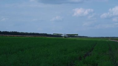 Lightweight airplane landing on airfield with spinning propeller turning off engine. White ultralight plane parking on green grass countryside after training flight. Aircraft moving against blue sky.