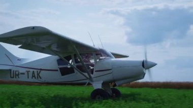 Small ultralight airplane takeoff from green grass farmland. White propeller plane accelerating speed flying on airfield against blue cloudy sky. Professional aviator riding modern air transport.