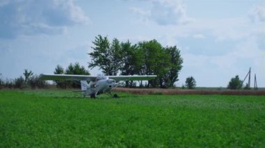 Small countryside airplane stopping on green grass airfield going to parking. Lightweight white plane with spinning propeller landing on beautiful field turning off engine. Aviation hobby concept.