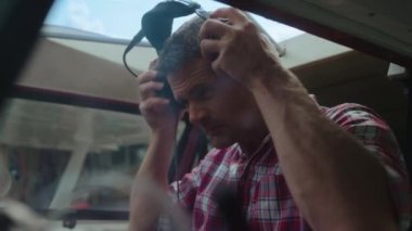 Airplane pilot preparing for flight putting on headphones sitting private plane cabin close up. Professional man aviator checking connection headset in modern aircraft. Piloting hobby concept.