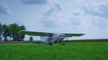 Ultralight private airplane preparing to taking off on green airfield summer day. White flight vehicle with spinning propeller standing in front beautiful cloudy sky. Skydive training concept.