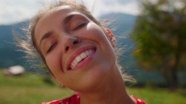 Closeup happy woman face with bright smile posing in mountains. Portrait of cheerful girl enjoying sunlight standing valley in summer holiday. Smiling lady looking camera on green meadow sunny day.