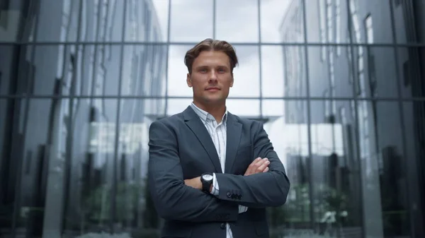 Confident businessman posing at office portrait. Successful corporate people. Ambitious man financial expert standing alone in suit look in camera downtown. Dressed handsome investor smiling outdoors.