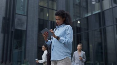 Şehir merkezinde tablet bilgisayar kullanan gülümseyen bir kadın. Şirket çalışanları gidiyor. Neşeli Afrikalı Amerikalı kız kontrol mailine dokunuyor. Kendine güvenen yönetici oturum açıyor. Sabah işyerine git.