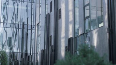 Dışarıdaki modern cam ofis binası. Gökyüzünden geçen arabayı yansıtan büyük panorama pencereleri. Arka bahçesinde temiz yeşil peyzaj olan kentsel iş bölgesi. Avrupa Yatırım Merkezi dış görünüş