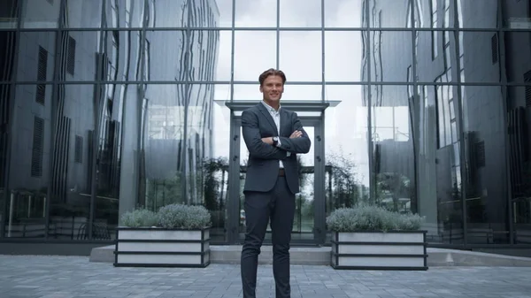 Smiling financial consultant standing at modern office portrait. Success concept. Attractive man startup ceo posing outdoors look in camera. Confident businessman enjoying triumph of sales project.