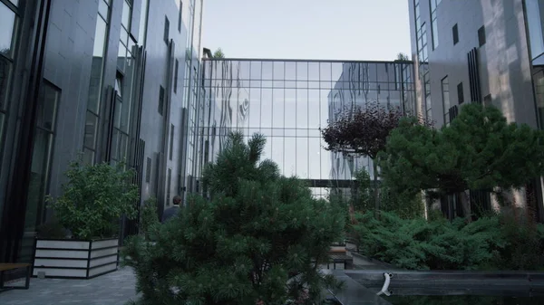 Modern glass office complex with neat landscaped garden. Futuristic architecture. Unknown man assistant walking empty recreation place in suit. European business center building with panorama windows