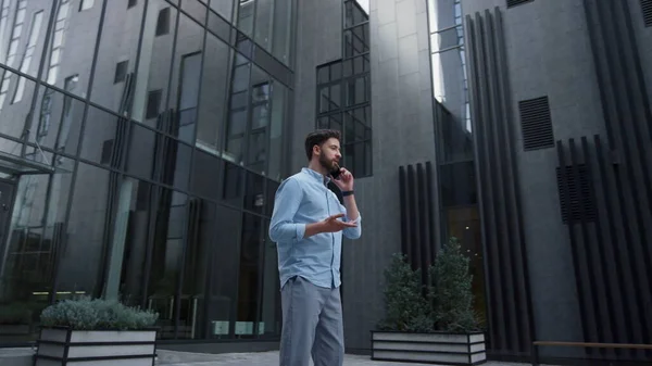 Attractive man speaking phone at modern glass building. Confident businessman successful ceo talking smartphone with partners discussing project. Handsome bearded manager working outside office.