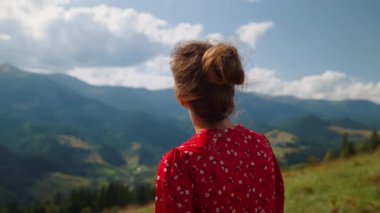 Back view of tranquil young girl standing green hill stretching neck sunny day close up. Unknown woman admiring mountain scenery under cloudy sky. Relaxed lady spending summer vacation alone on nature