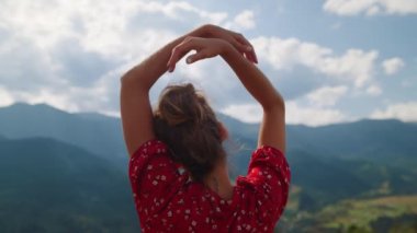 Back view of carefree woman holding hands over head relaxing on nature close up. Unrecognizable girl spending summer vacation in mountains. Unknown model relaxing standing on green hill sunny day.
