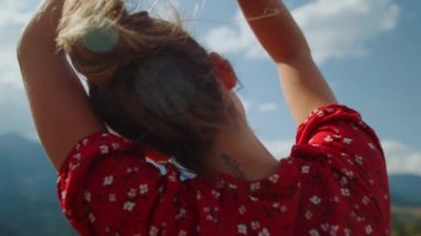 Unknown woman raising hands to sky relaxing outdoor close up. Back view of tranquil girl moving arms in front clouds. Carefree calm lady enjoying summer holiday in mountains. Nature beauty concept