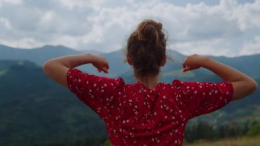 Unrecognizable girl raising hands watching beautiful gloomy mountains scenery close up. Back view of young woman resting on nature summer cloudy day. Unknown model enjoying tranquility at holiday.