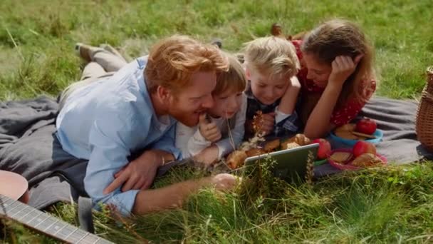 Happy Family Watching Video Tablet Computer Lying Green Grass Cheerful — Stockvideo