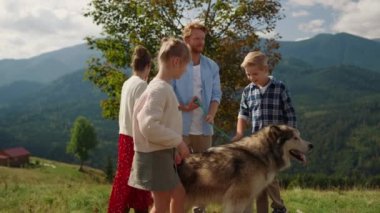Friendly people walking fluffy dog on green hill sunny day. Redhead man keeping husky on leash standing green grass mountain slope. Cheerful family enjoying holiday with fluffy pedigree pet outdoor.