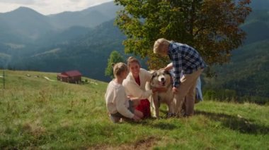 Cute family feeling happy with beloved dog on mountains slope. Smiling mother with blond son caressing adorable furry husky on summer walk sunny day. Happy people relax on nature with lovely pet.