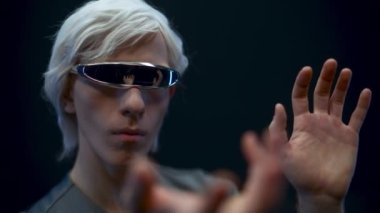 Smart man touching invisible interface in VR glasses closeup. Blonde gamer playing surrounded with futuristic metaverse nft 3d data black background. Augmented reality, future technology concept
