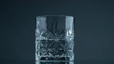 Waving water liquid glass at dark background closeup. Mineral fluid splashing mixing in beautiful crystal cup. Transparent mineral beverage rippling for commercial shot. Beautiful simplicity concept