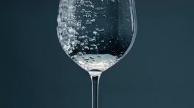 Air bubbles rising glass closeup. Pure mineral water pouring transparent cup at dark background. Drinking fluid refreshing beverage filling beautiful clear glassware. Wellness hydration concept.