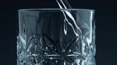 Closeup water pouring glass with splashing dark background. Crystal fresh liquid filling beautiful transparent cup. Clear mineral water flowing textured container. Cool refreshing beverage concept.