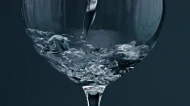 Closeup pure water filling wine glass. Air bubbles rising up from cup bottom. Beautiful refreshing beverage pouring splashing in transparent container. Purified drinking fluid flowing clear glassware.