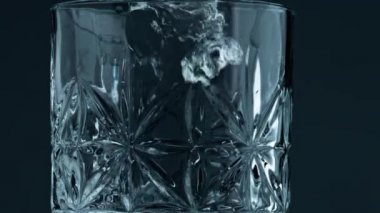 Closeup glass filling water at dark background. Transparent droplets falling splashing into textured container. Beautiful shot of clear still fluid pouring into crystal jug. Hydration thirst concept.