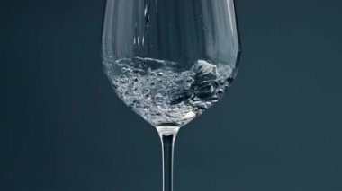 Clear water filling cup closeup. Pure refreshing beverage pour into transparent glass at dark background. Beautiful shot of purified liquid falling in crystal container. Bubbles rising glassware.